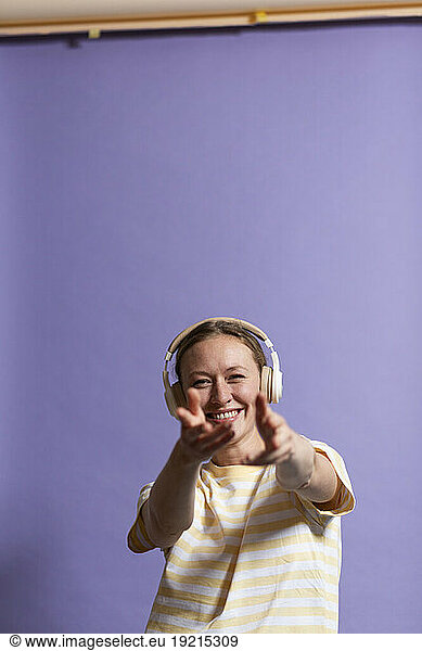 Happy woman listening music and dancing against purple background
