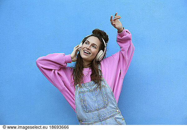 Happy woman listening to music and dancing against blue background