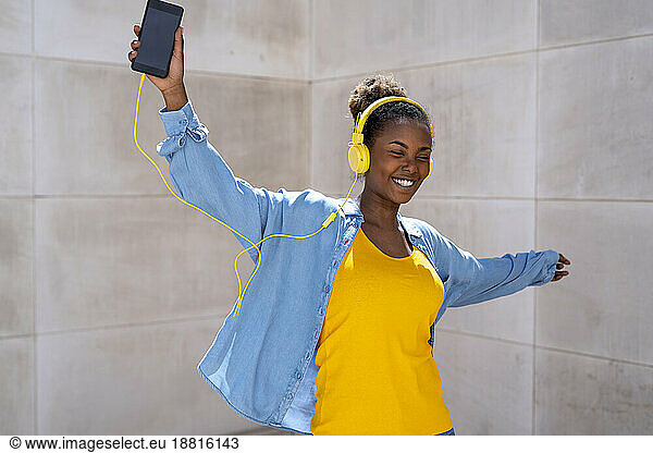 Happy woman listening to music near wall