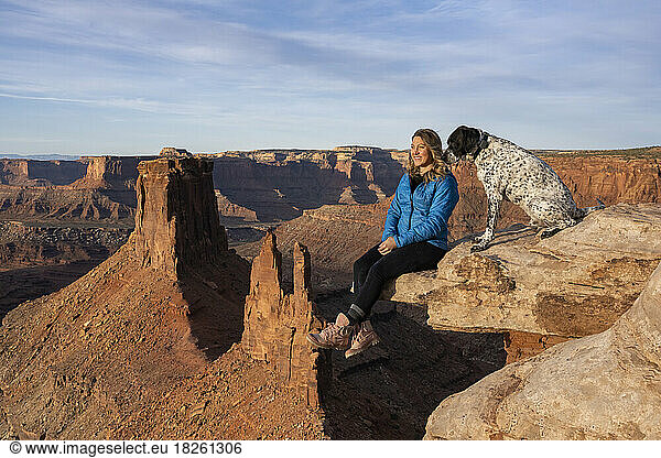 Happy woman looking at view while sitting by dog on edge in desert