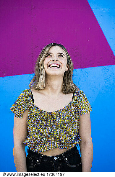 Happy woman looking up while standing in front of colorful wall
