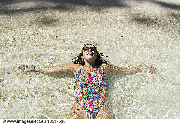 Happy woman lying down in water at beach