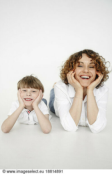 Happy woman lying down with son in front of white backdrop