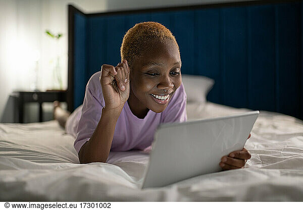 Happy woman lying on bed and having video call on tablet