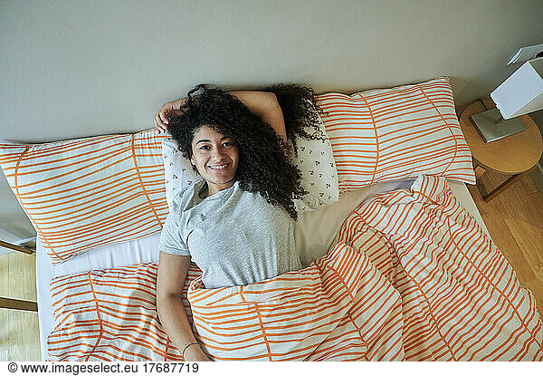 Happy woman lying with hand behind head on bed at home