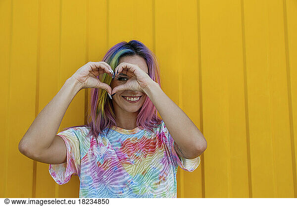 Happy woman making heart shape with hands in front of yellow wall