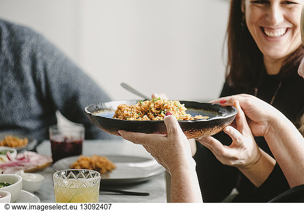 Happy woman passing rice plate to friend while sitting at table