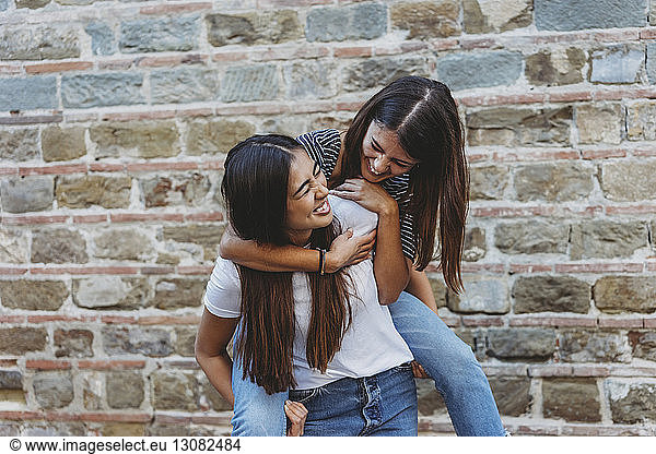 Happy woman piggybacking friend while standing by building