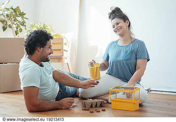 Happy woman planting seeds in seedling tray with man lying on floor