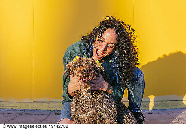 Happy woman playing with water dog in front of yellow wall