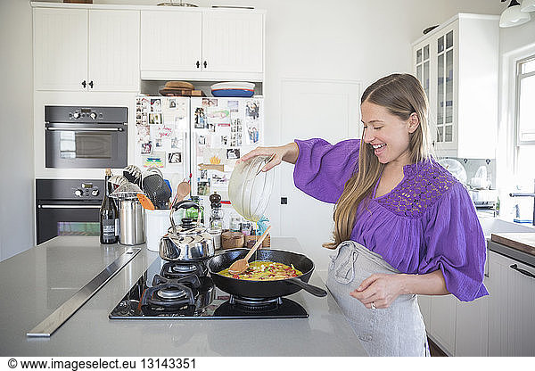 Happy woman pouring batter in cooking pan at kitchen