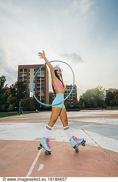 Happy woman practicing roller skating with hoop at sports court