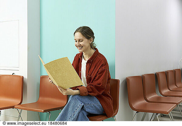 Happy woman reading medical results sitting on chair at clinic