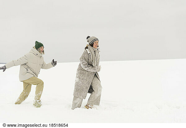 Happy woman running behind friend having fun in snow