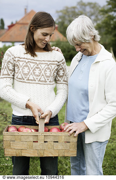 Happy woman showing apple basket to mother in back yard