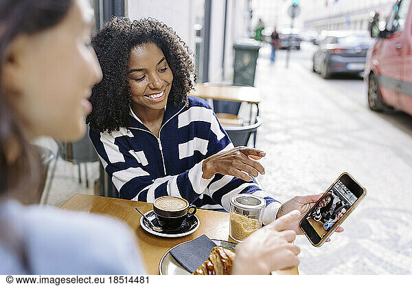 Happy woman showing photographs on smart phone to friend