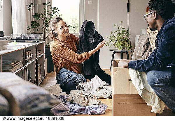 Happy woman showing shirt to man while sorting clothes at home