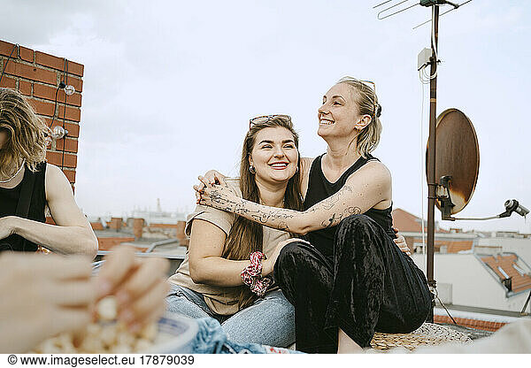 Happy woman sitting arm around with female friend on rooftop
