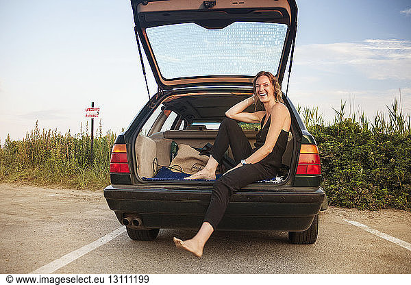 Happy woman sitting in open car trunk on road