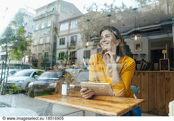 Happy woman sitting tablet PC seen through glass