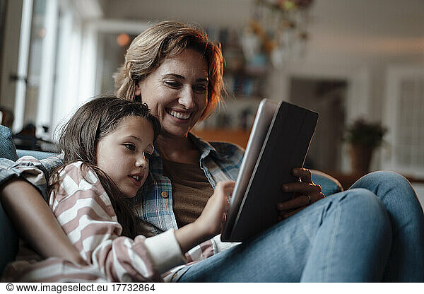 Happy woman sitting with daughter using tablet PC at home