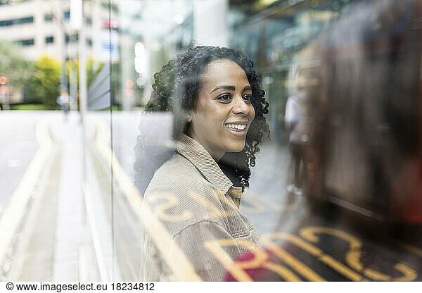 Happy woman sitting with friend at bus stop seen through glass
