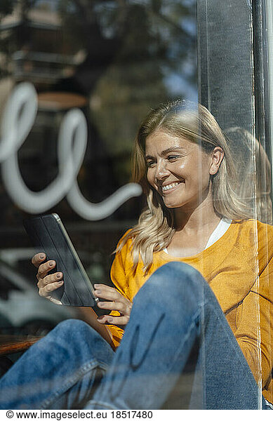 Happy woman sitting with tablet PC near window in cafe