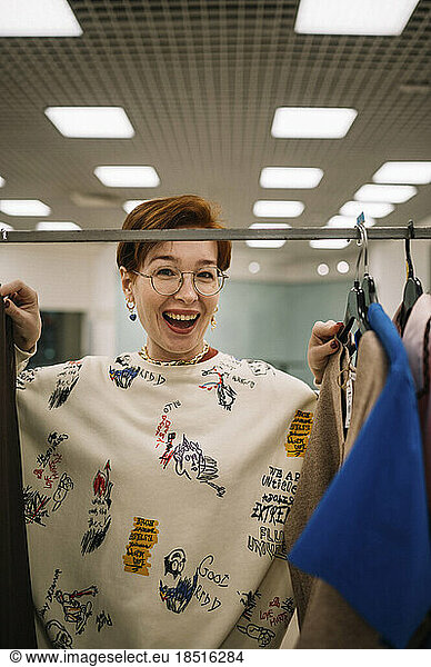 Happy woman standing by clothing rack