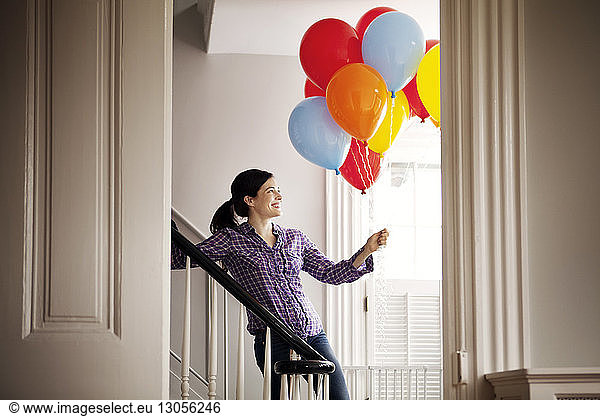 Happy woman standing by staircase while holding helium balloons