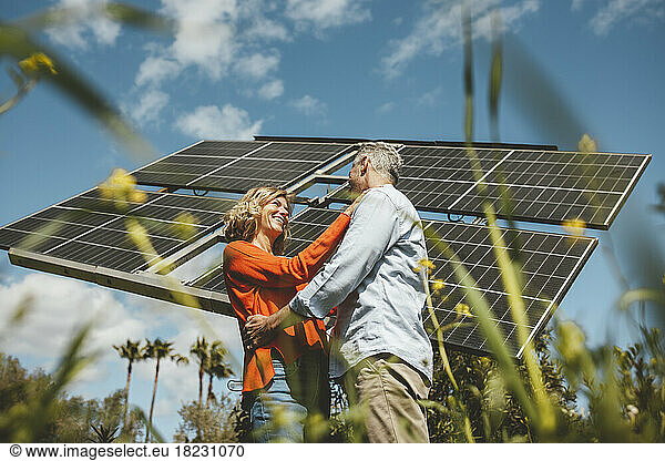 Happy woman standing with man by solar panels in garden