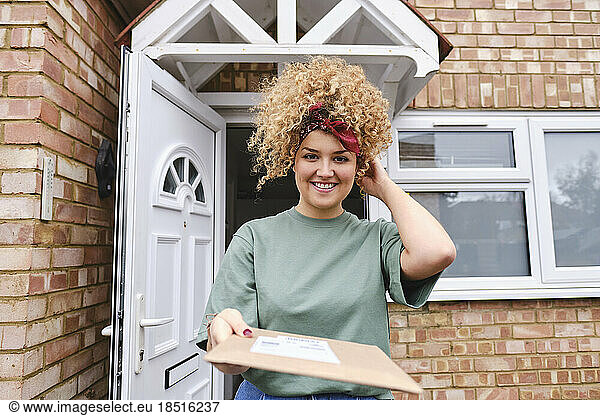 Happy woman standing with package in front of house