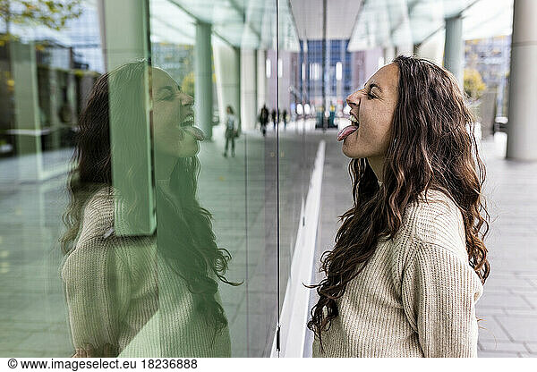 Happy woman sticking out tongue looking at reflection on glass wall