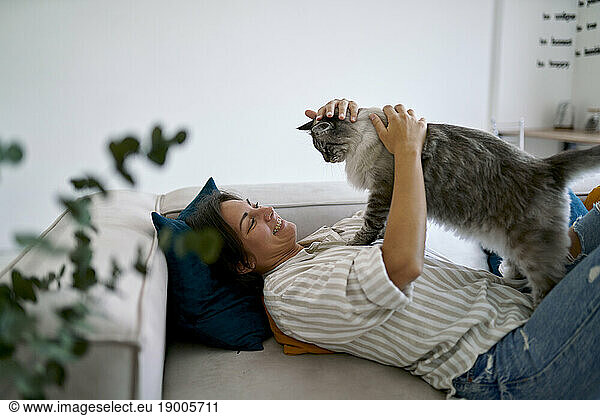Happy woman stroking and playing with cat at home