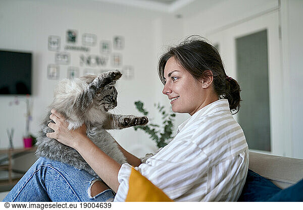 Happy woman stroking cat on sofa at home