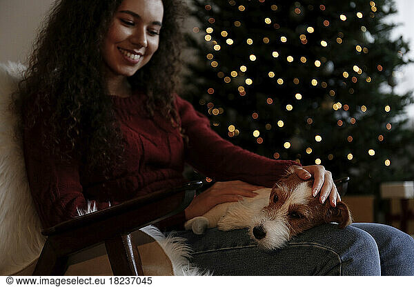 Happy woman stroking dog sitting in armchair at home