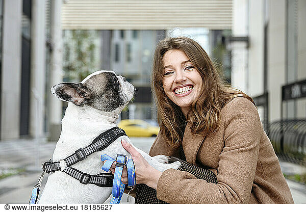 Happy woman stroking french bulldog at footpath