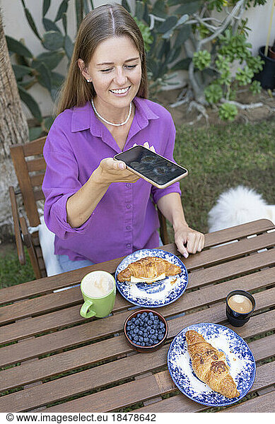 Happy woman taking selfie of croissants on table in garden