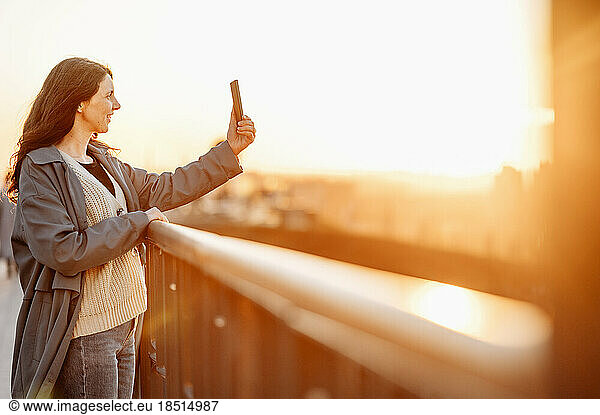 Happy woman taking selfie on bridge at sunset