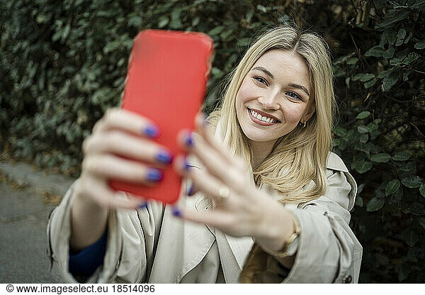 Happy woman taking selfie through mobile phone near plants