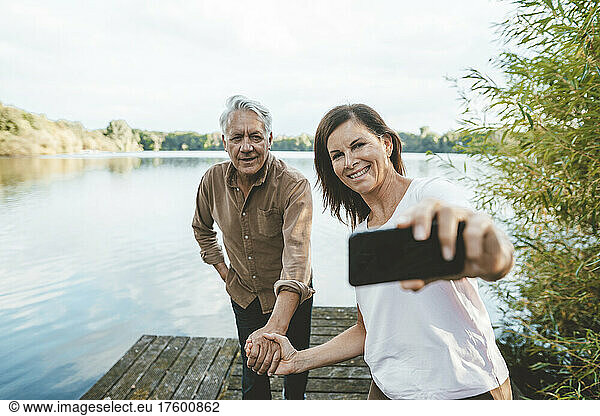Happy woman taking selfie through smart phone with senior man on jetty
