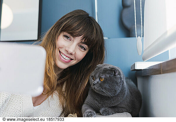 Happy woman taking selfie with cat at home