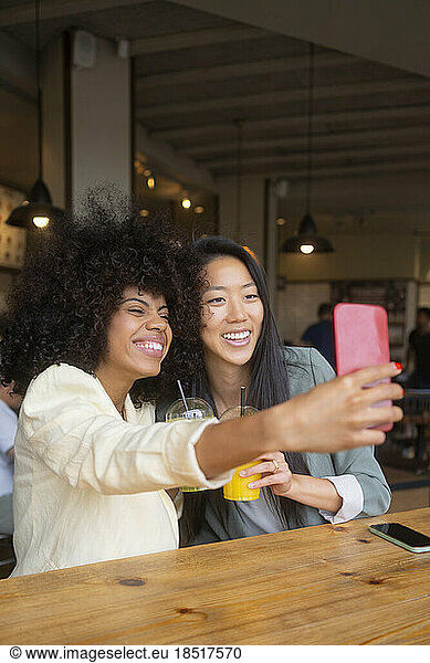 Happy woman taking selfie with friend at cafe