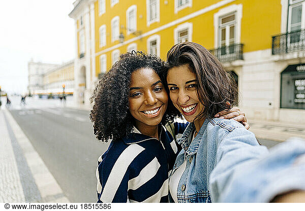 Happy woman taking selfie with friend in front of yellow building