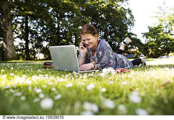 Happy woman talking on phone and using laptop at park