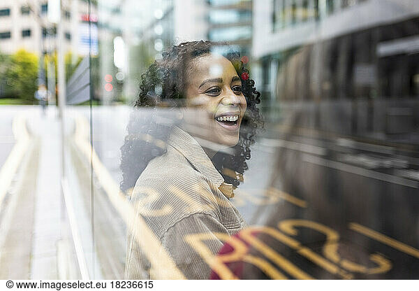 Happy woman talking to friend at bus stop seen through glass