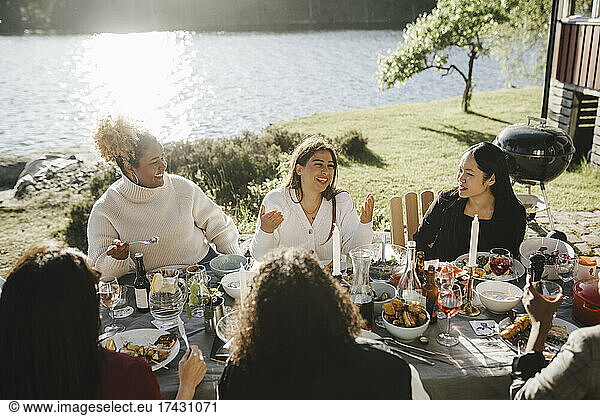 Happy woman talking with female friends while enjoying dinner party at back yard on sunny day