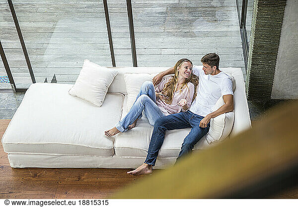 Happy woman talking with man sitting on sofa at home