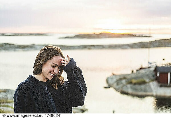 Happy woman touching forehead while looking down by sea