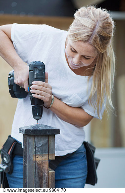 Happy woman using cordless screwdriver on wooden post