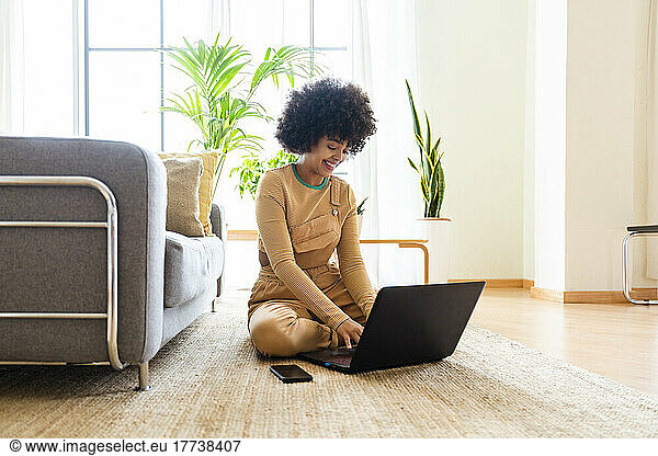 Happy woman using laptop sitting on carpet at home